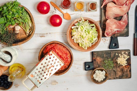 Fresh ingredients are arranged on a wooden table for cooking rabbit stew. There are tomatoes,