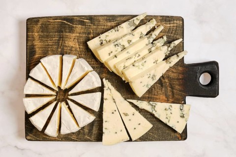 Different types of cheese are arranged on a wooden board. One cheese is round and cut into wedges.