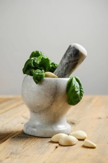 Fresh basil leaves and garlic cloves are placed in a mortar. A pestle is ready to crush the