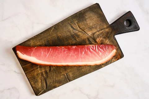 A long piece of cured parma ham on a wooden cutting board. The board has a rustic design and is