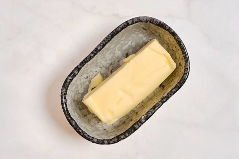 A piece of butter in a grey dish on a white countertop. This setting shows a kitchen environment