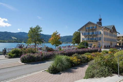 Historic town hall, tourists on the promenade on the banks of Tegernsee, flower beds in the
