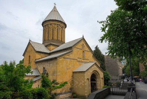 Historic church with yellow stone architecture and dome surrounded by trees on a cloudy day, Sioni