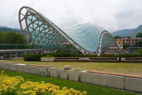 Modern glass roof of a bridge in wave form with surrounding park area, Peace Bridge, Rike Park,