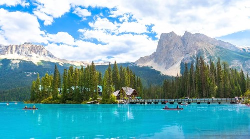 Canoeing tourists glide across the turquoise waters of emerald lake, framed by a wooden bridge,