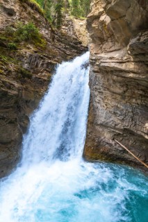 Powerful waterfall plunging into a vibrant turquoise pool in johnston canyon, creating a