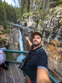 Tourist taking a selfie with outstretched arm at johnston canyon lower falls, showcasing the