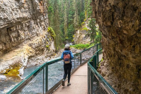 Female tourist with backpack walking on a metal catwalk enjoying the scenic view of johnston canyon