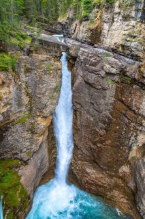 Cascading waterfall pouring into a vibrant turquoise pool amidst the rugged johnston canyon in