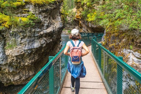 Female tourist with backpack walking on metal catwalk enjoying the view of johnston canyon and the