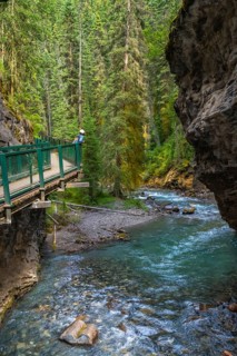 Turquoise water flows through johnston canyon in banff national park as a tourist walks on the