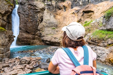 Female tourist wearing a backpack and baseball cap admiring a stunning waterfall cascading into