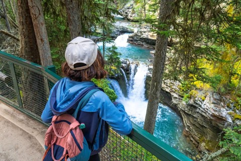 Female hiker wearing backpack and cap admiring cascading waterfalls and turquoise water of johnston