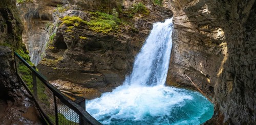 Powerful waterfall cascading into a turquoise pool in johnston canyon, surrounded by rocky cliffs