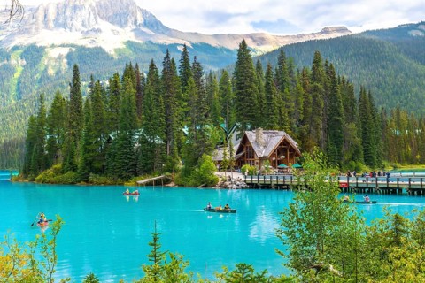 Tourists are canoeing on the turquoise waters of emerald lake with a beautiful wooden lodge and the