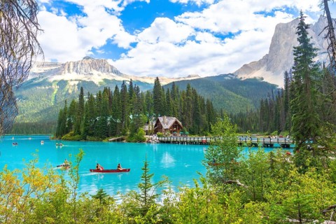 Canoeing tourists navigate the turquoise waters of emerald lake, with a wooden lodge and bridge set