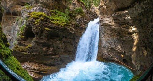 Sunlight illuminating the vibrant turquoise pool at the base of a cascading waterfall in johnston