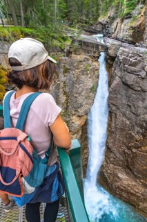 Female tourist carrying a backpack and baby carrier, enjoying the stunning view of a waterfall