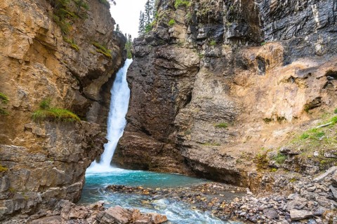 Cascading waterfall flowing into a vibrant turquoise pool in johnston canyon, surrounded by rugged