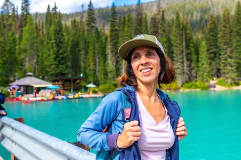 Female hiker wearing a baseball cap and backpack standing near the turquoise waters of emerald