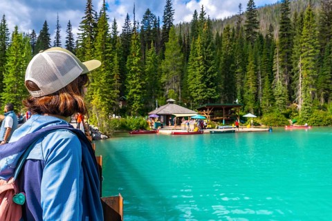 Tourist standing on a bridge admires the turquoise waters of emerald lake, surrounded by lush