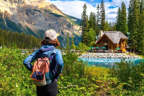 Tourist with a backpack is enjoying the breathtaking view of emerald lake and its charming wooden