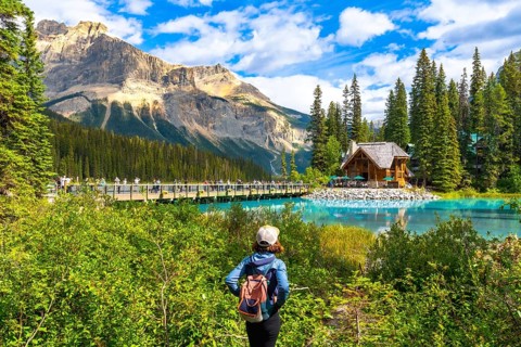 Female tourist with a backpack admiring breathtaking turquoise waters of emerald lake, featuring an