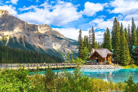 Wooden lodge sitting on the shore of a turquoise lake reflecting the surrounding lush vegetation
