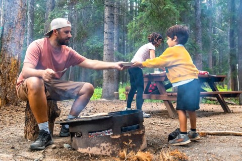 Father serving food to children at campsite, cooking on campfire in banff national park, canadian