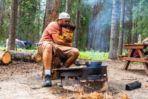 Father showing affection to his son while cooking breakfast on campfire during a camping trip in