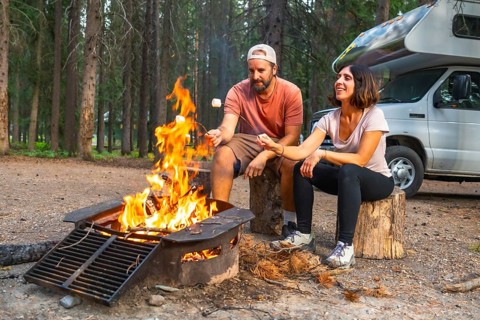 Tourists roasting marshmallows over a cozy campfire near their campervan, surrounded by the
