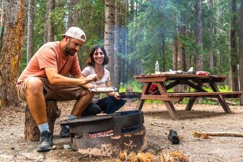 Tourists enjoying the warmth of a campfire while cooking delicious meals during their camping