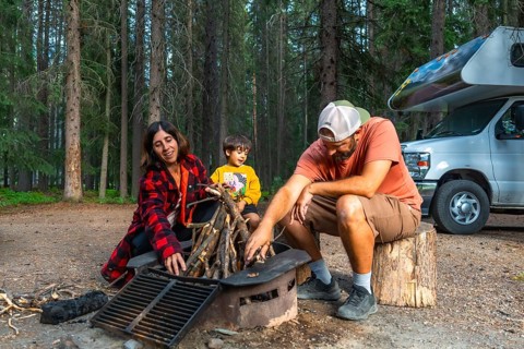 Family with little boy making campfire near their campervan during their vacation camping in the