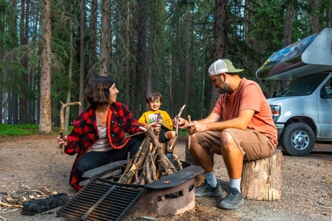 Family enjoying camping in the canadian rockies, preparing campfire next to their campervan in