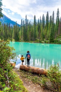Tourists standing on a log are enjoying the breathtaking view of the turquoise water of emerald