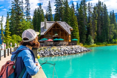 Female hiker admiring the turquoise waters of emerald lake and its charming lodge, nestled among