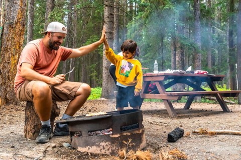 Father and son are giving a high five while grilling food over a campfire, enjoying quality time