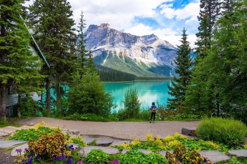 Tourist with a backpack admiring the breathtaking turquoise waters of emerald lake and the imposing
