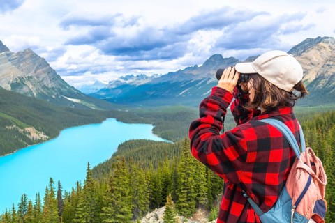 Female hiker using binoculars admires the stunning turquoise waters of peyto lake and majestic