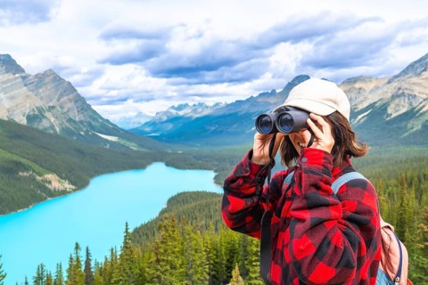 Female hiker using binoculars, admiring the scenic turquoise waters of peyto lake and the majestic