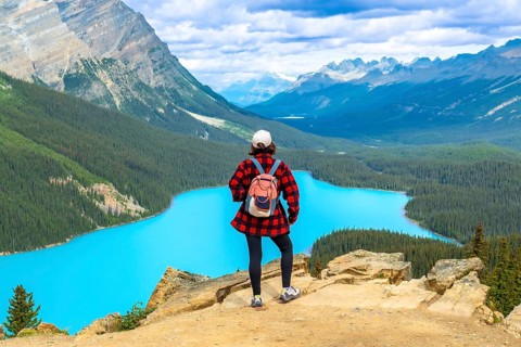 Female hiker standing on a cliff, soaking in the stunning panoramic view of turquoise peyto lake
