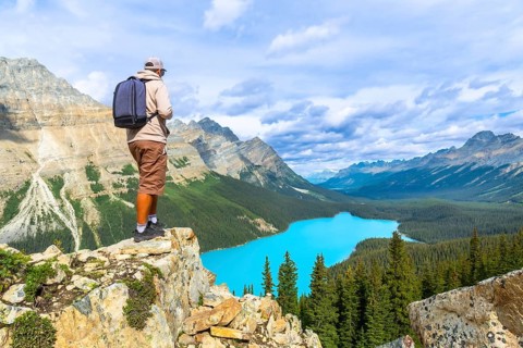 Hiker standing on a cliff edge, soaking in the breathtaking panoramic views of turquoise peyto