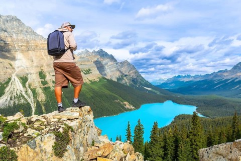 Photographer standing on a rocky cliff captures a breathtaking view of turquoise peyto lake