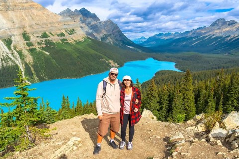 Two hikers are standing on a mountaintop, enjoying the breathtaking panoramic view of the turquoise