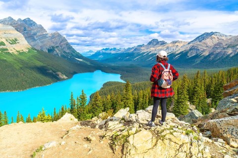 Female tourist with backpack standing on a rocky cliff overlooking the stunning turquoise waters of