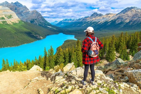Female hiker wearing a backpack, standing on a rocky viewpoint and admiring the stunning turquoise