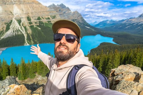 Hiker taking a selfie with outstretched arms, embracing breathtaking turquoise waters of peyto