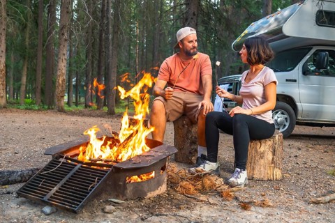 Tourists roasting marshmallows over campfire near their campervan, enjoying a peaceful evening in