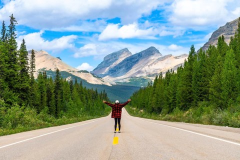 Female tourist standing on a scenic road with open arms, enjoying the freedom and breathtaking view