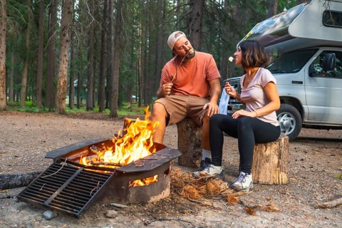 Tourists roasting marshmallows in a campfire near their campervan, enjoying a relaxing evening in